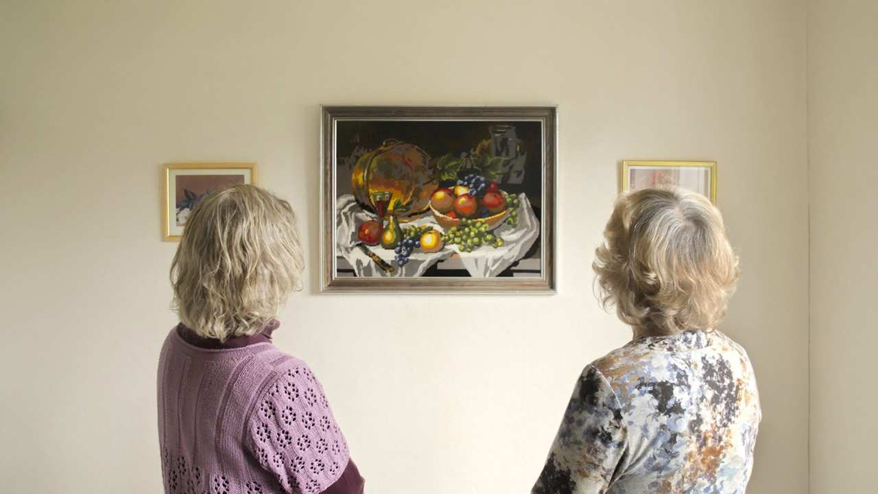 two women looking at a painting of a bowl of fruit